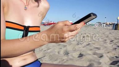 穿比基尼的女人在海滩上用智能手机发短信。 户外使用智能手机特写双手。 移动